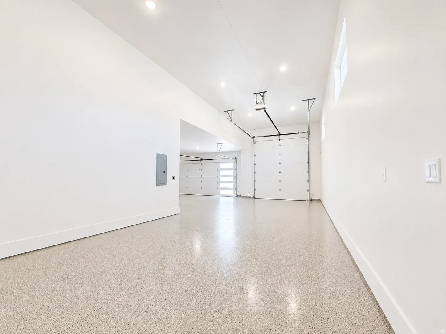 Spacious garage featuring a speckled epoxy floor, white walls, recessed lighting, and multiple garage doors including one with frosted glass panels