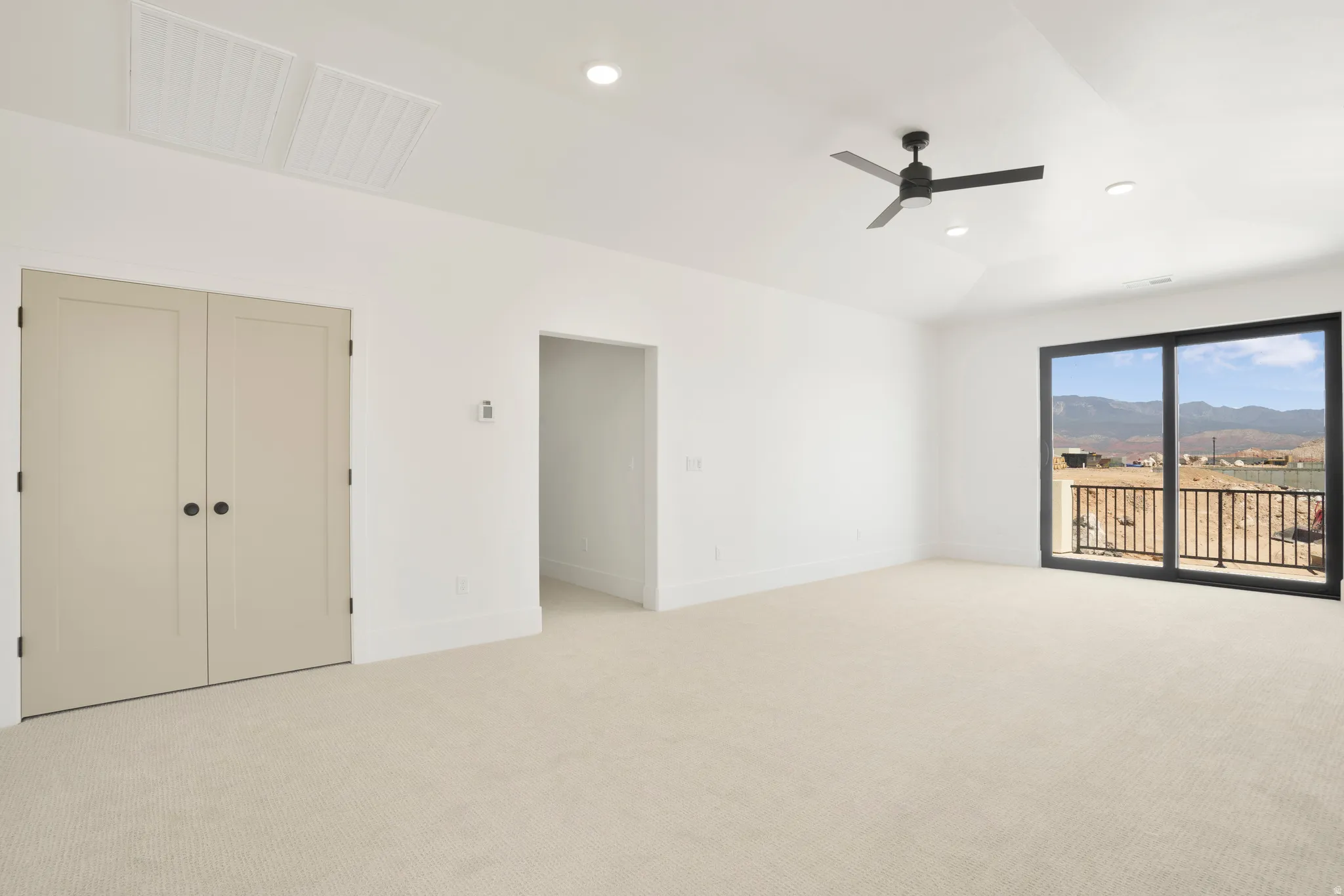 Expansive room featuring light-toned carpeting, a large sliding glass door, and a black metal balcony railing