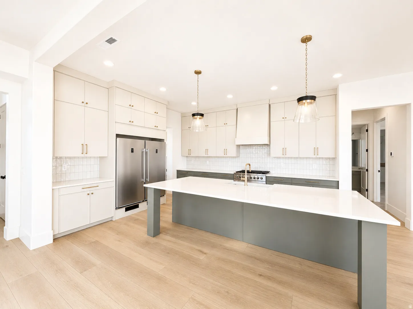 Open-concept kitchen featuring light wood-finish flooring, a central island with a white countertop and contrasting base, and pendant lighting