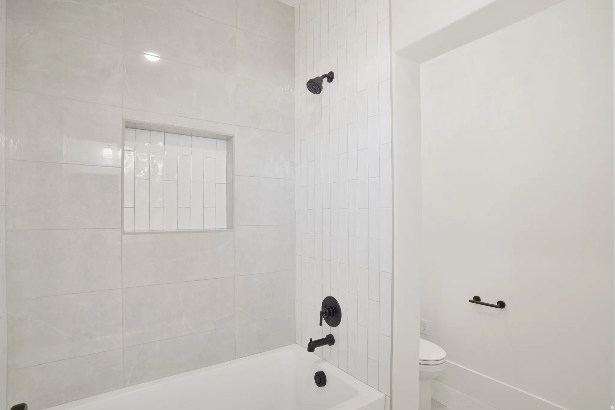 Bathtub with matte black fixtures, an integrated shower niche with vertical subway tile, and large format wall tiling