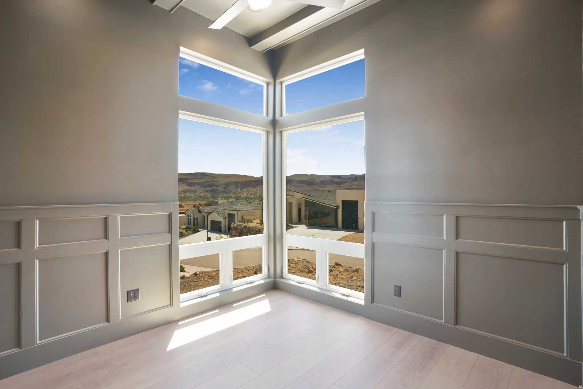 Corner window array with panoramic desert scenery, featuring contemporary paneling, vaulted ceiling, and wood-finish flooring