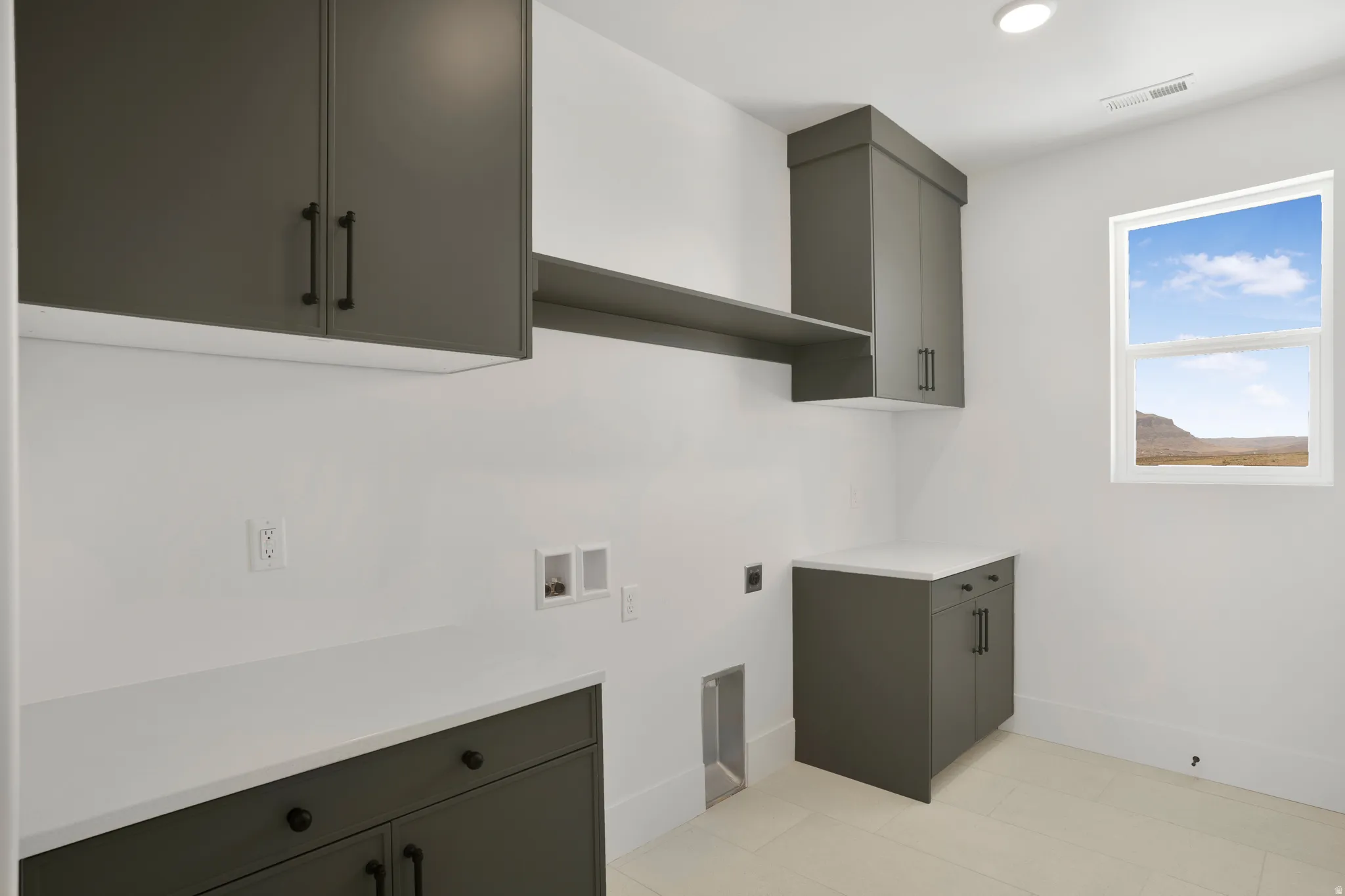 Laundry area featuring dark gray cabinetry with matte black hardware, white countertops, a built-in shelf, and a window providing natural light