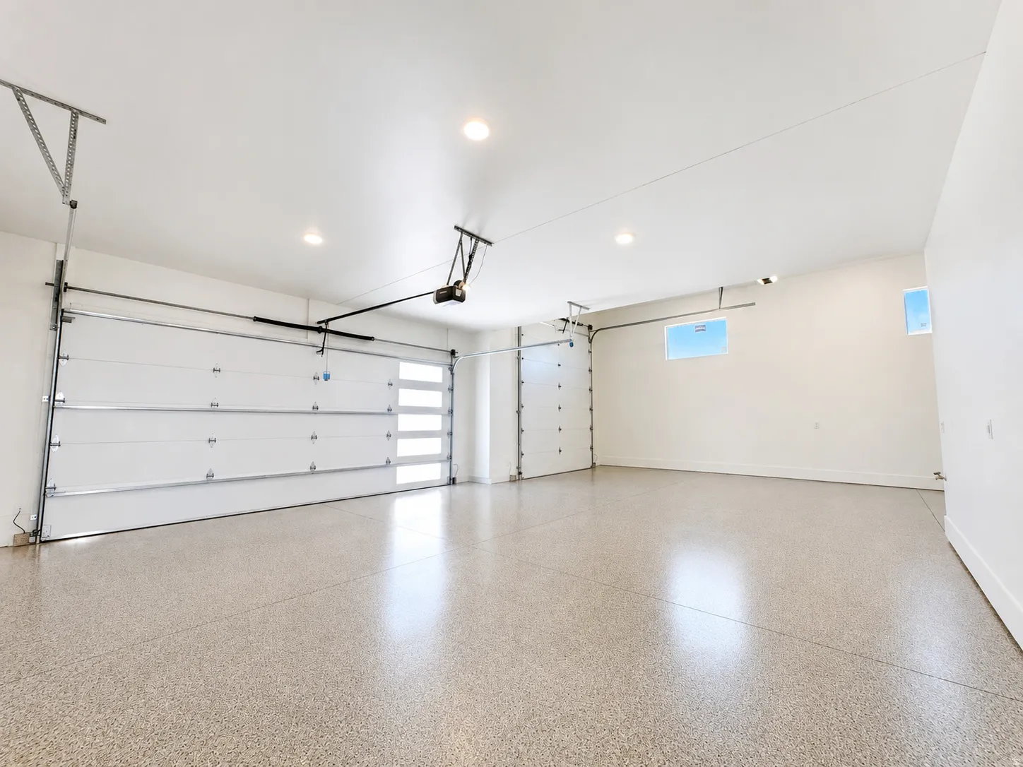 Spacious garage featuring a durable epoxy floor finish, two overhead garage doors, recessed lighting, and high-set windows providing natural light