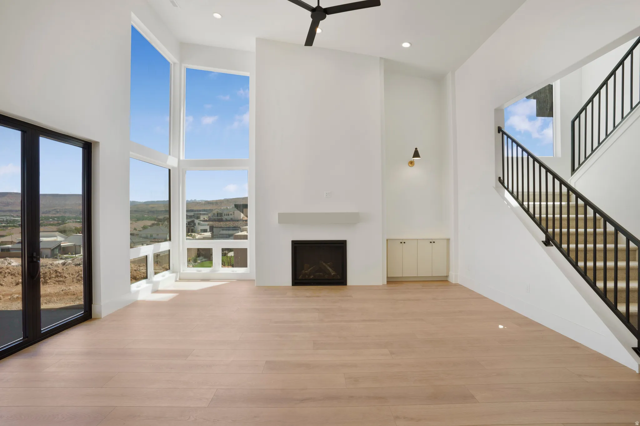 Two-story living area featuring extensive window walls, light wood-finish flooring, and a contemporary fireplace with a white mantle