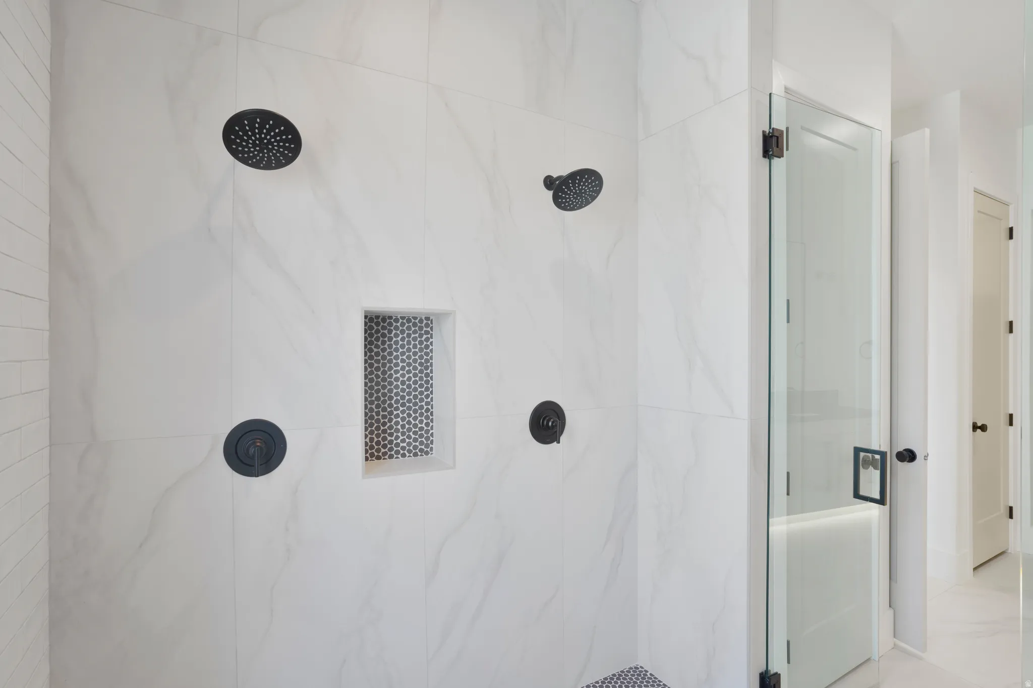 Spacious shower featuring white tiled walls, dual matte black rain showerheads, a built-in niche with mosaic tile, and a frameless glass enclosure
