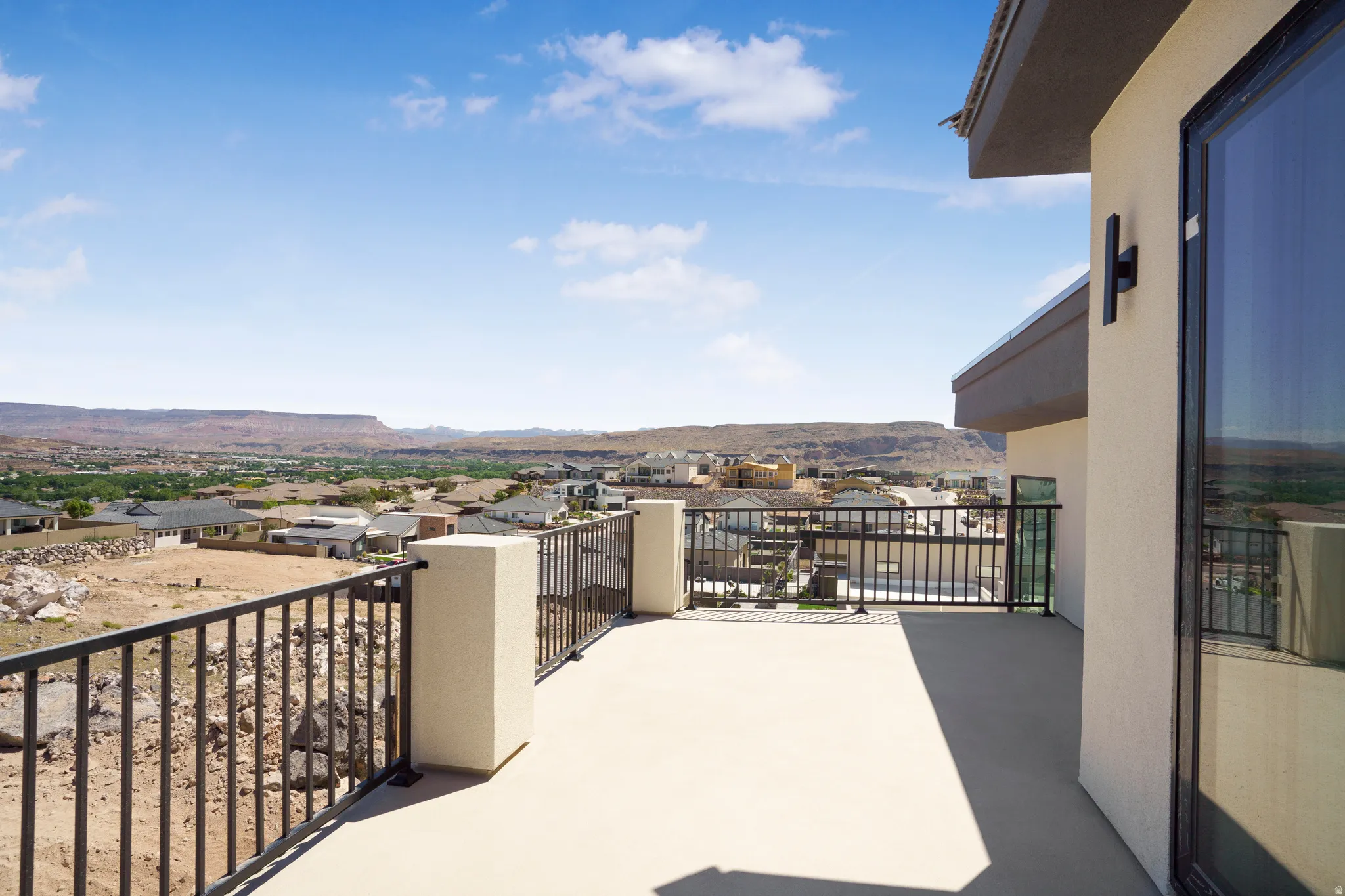 Expansive elevated balcony featuring stucco pillars, black metal railings, and a wide-format glass door