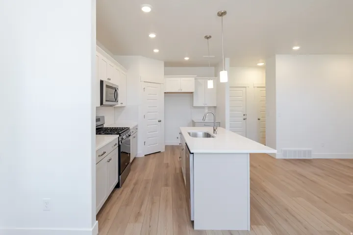Kitchen featuring stainless steel appliances, white cabinetry, a kitchen island with sink, pendant lighting, and wood-finish flooring