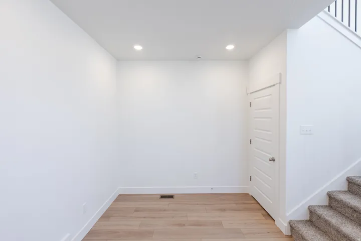 Recessed ceiling lighting, wood-finish flooring, paneled interior door, and carpeted stairs with a metal baluster
