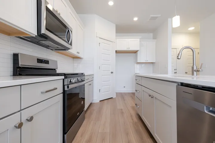 Modern kitchen featuring white cabinetry, light wood-finish flooring, stainless steel appliances, a subway tile backsplash, and light-toned countertops