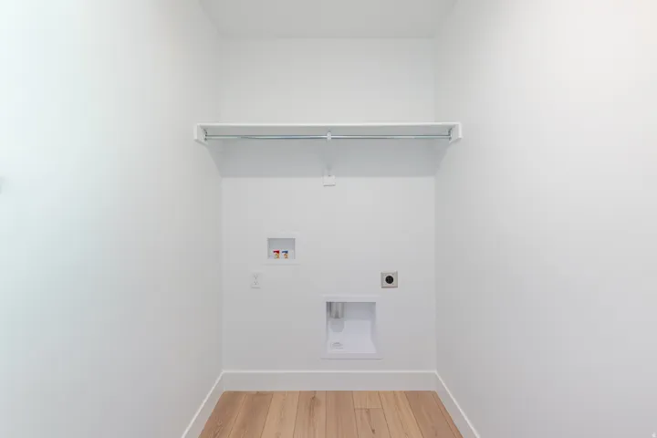 Dedicated laundry area featuring a built-in shelf, hanging rod, and wood-finish flooring
