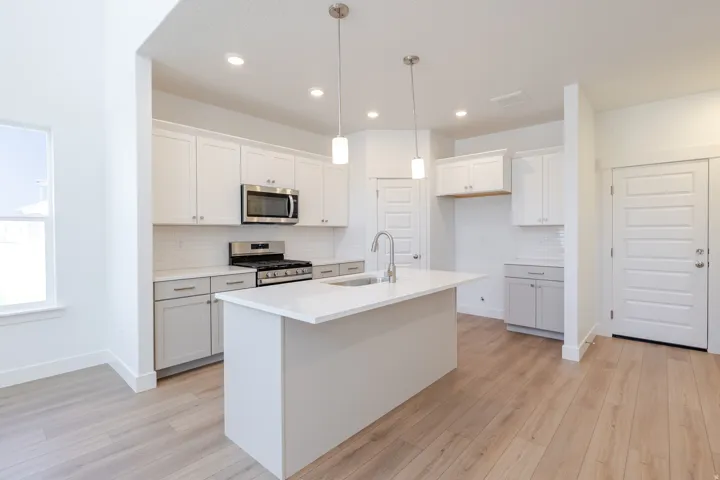 Modern kitchen featuring white shaker cabinetry, stainless steel appliances, a center island with sink, white countertops, and wood-finish flooring