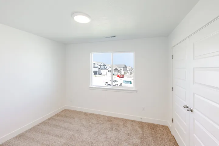 Neutral-toned carpet flooring, white walls, flush-mount ceiling light fixture, white-framed window, and white paneled doors