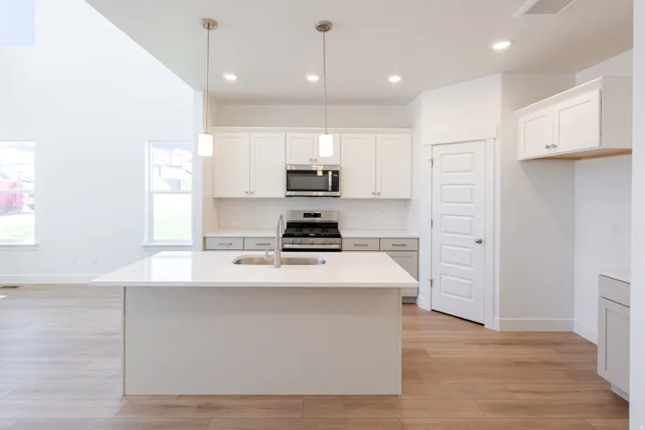Modern kitchen featuring a central island with an undermount sink, white cabinetry, stainless steel appliances, and light wood-finish flooring
