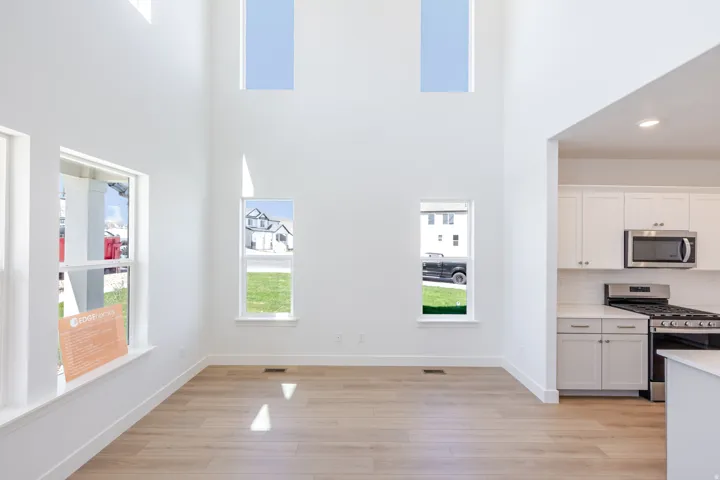 Two-story ceiling height with multiple windows, wood-finish flooring, white cabinetry, stainless steel appliances, and subway tile backsplash