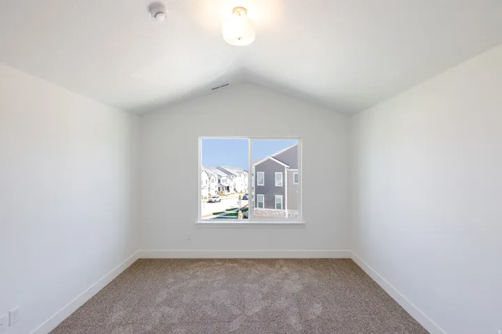 Vaulted ceiling with an overhead light fixture, neutral carpet, and a large window