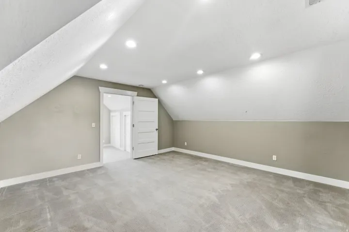 Spacious room featuring sloped ceilings, recessed lighting, and soft gray carpeting