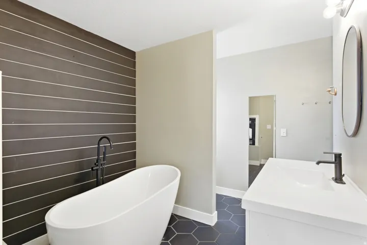 Bathroom featuring a freestanding tub with a floor-mounted matte black faucet, a dark horizontal tile accent wall, hexagonal floor tiling, a white vanity with an integrated sink, and a matte black single-handle faucet