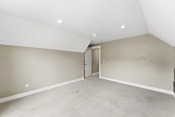 Spacious room featuring sloped ceilings, recessed lighting, neutral wall tones, and light-toned carpeting