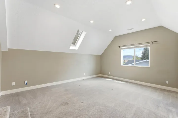 Spacious room featuring vaulted ceilings, a skylight, recessed lighting, and a large window