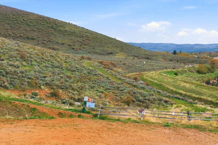 Expansive undeveloped land featuring a gentle slope, natural vegetation, and distant mountain scenery