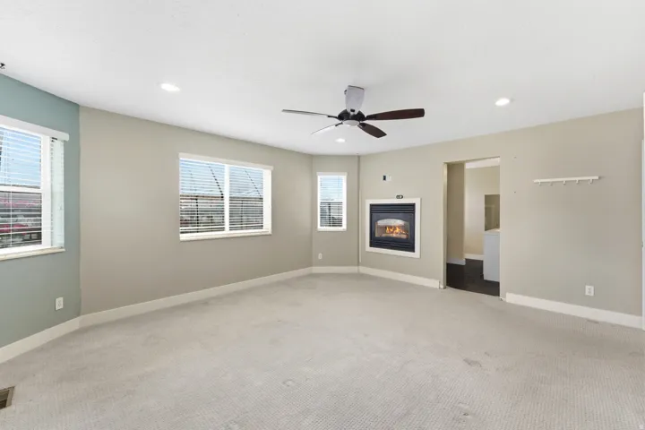 Spacious room featuring an inset fireplace with a white surround, recessed lighting, and a ceiling fan