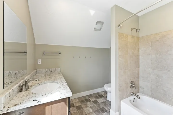 Bathroom featuring a white bathtub with tile surround, a vanity with a granite-style countertop, a white oval sink, and chrome fixtures