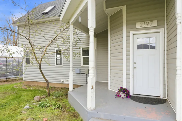 Front entry featuring a covered porch, white paneled door with windowpanes, and light-colored siding