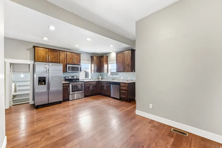 Open concept kitchen featuring wood-finish flooring, stainless steel appliances, dark wood cabinetry, recessed lighting, and a light-colored tile backsplash