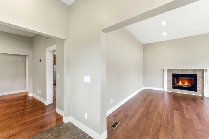 Vaulted ceiling living area featuring wood-finish flooring, a tile-surround fireplace with a white mantel, recessed lighting, and neutral wall tones