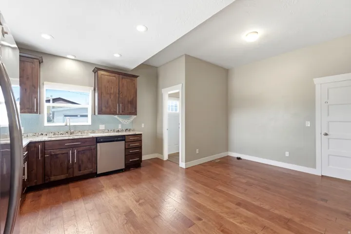 Open-concept kitchen and dining area featuring rich wood cabinetry, stainless steel appliances, speckled countertops, a blue tiled backsplash, and wood-finish flooring