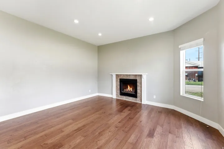 Living area featuring wood-finish flooring, a fireplace with a tiled surround and white mantel, recessed lighting, and a corner window