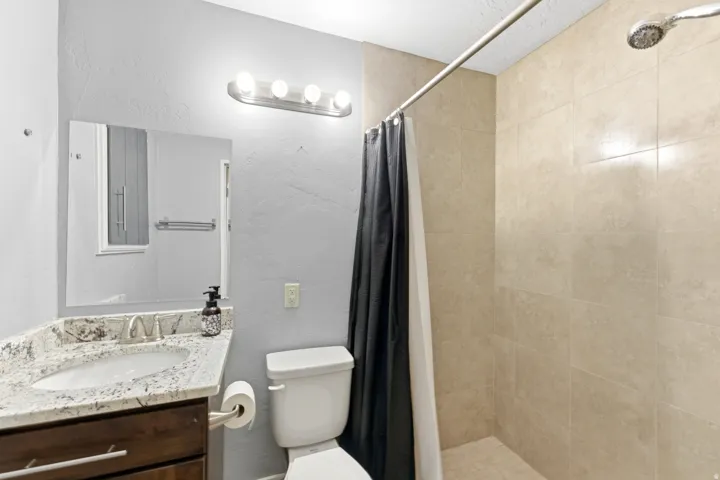 Bathroom featuring a walk-in shower with light-toned wall tiling, a vanity with a granite countertop, and a modern rectangular sink