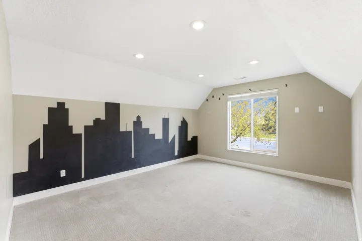 Bright room featuring a large window, sloped ceilings, recessed lighting, and a cityscape mural accent wall