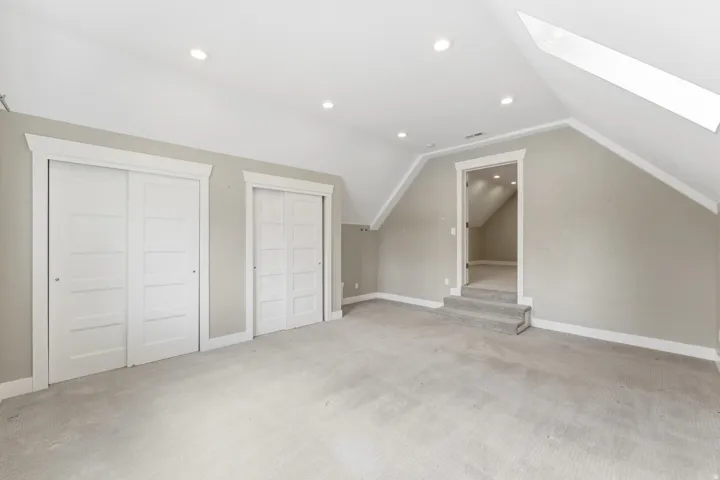 Carpeted room featuring two white sliding closet doors, recessed lighting, and an angled ceiling with a skylight