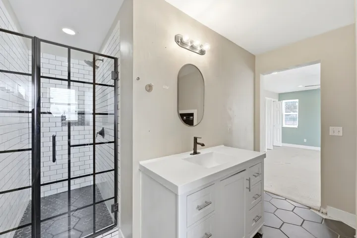Contemporary bathroom featuring a black-framed glass shower enclosure with white subway tile, a dark hexagon-tiled shower floor, and a white vanity with an undermount sink and matte black faucet