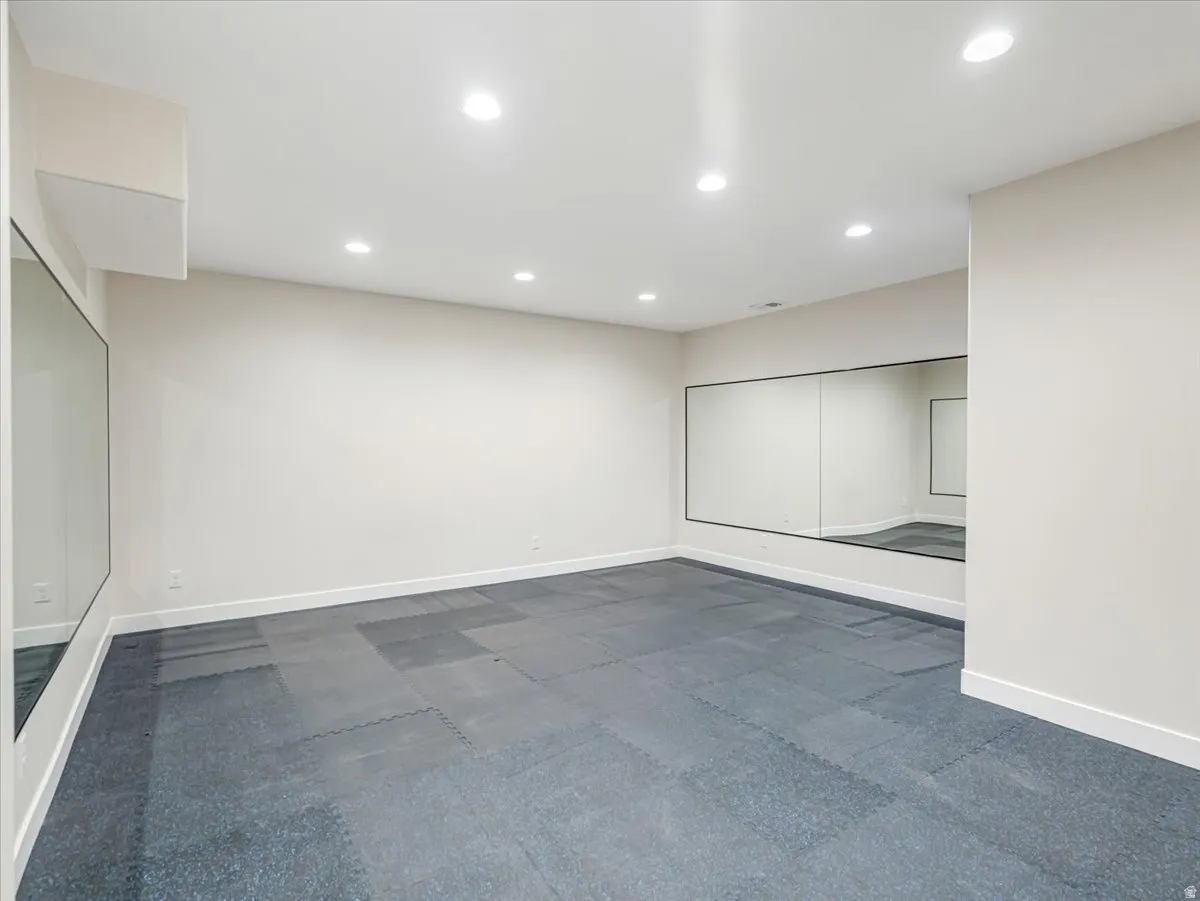 Spacious room featuring floor-to-ceiling wall mirrors, recessed lighting, and modular athletic flooring