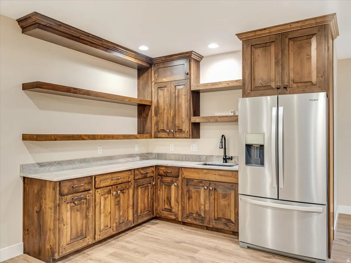 Functional corner kitchen area featuring rich wood cabinetry, light-toned countertop, a stainless steel refrigerator, and wood-finish flooring