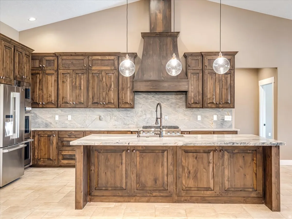 Gourmet kitchen featuring a large central island, distressed wood cabinetry, stainless steel appliances, a range hood, and pendant lighting