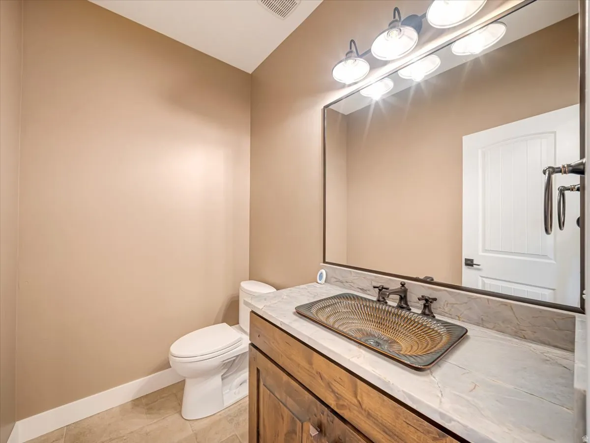 Bathroom featuring a unique vessel sink, a dark wood-finish vanity, a stone countertop, a large framed mirror, and a four-light fixture