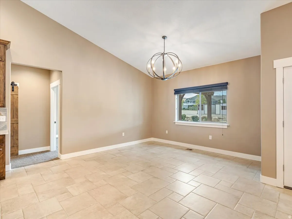 Spacious room featuring vaulted ceilings, large window with roller shades, and a contemporary spherical chandelier
