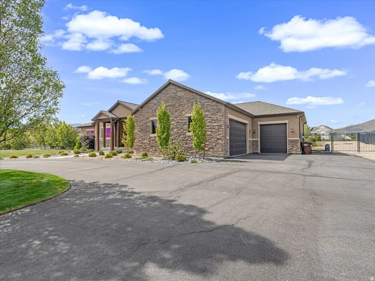 Stone and stucco exterior with multiple garage bays, a paved driveway, and established landscaping