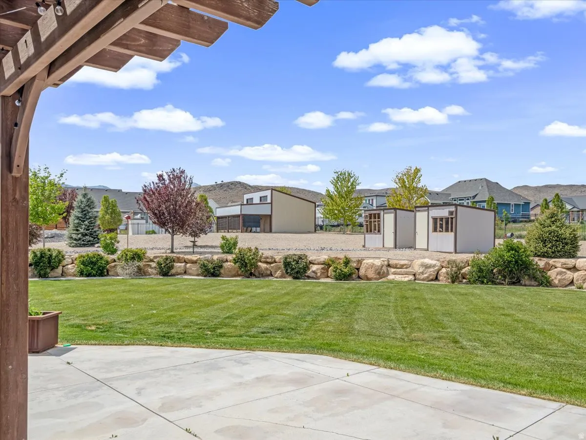 Expansive backyard featuring a concrete patio, a lush green lawn, a rock retaining wall, and mature landscaping