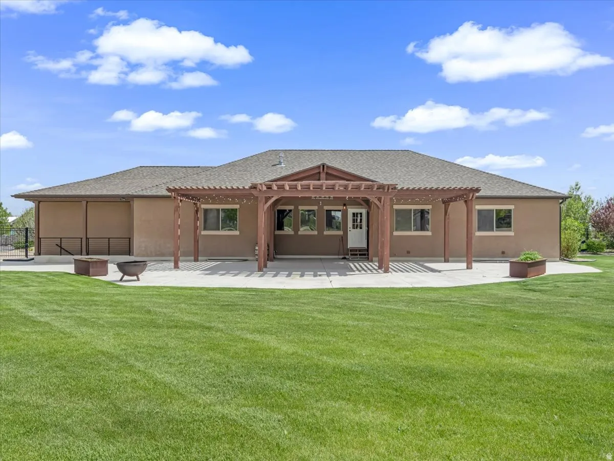Rear exterior with a concrete patio, wooden pergola, and expansive lawn