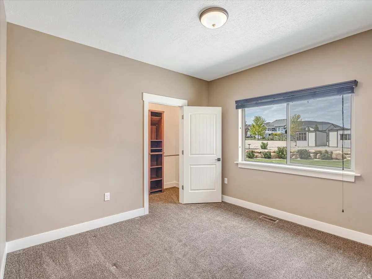 Carpeted room with a large window featuring roller shades, an interior door with vertical paneling, and a built-in closet system