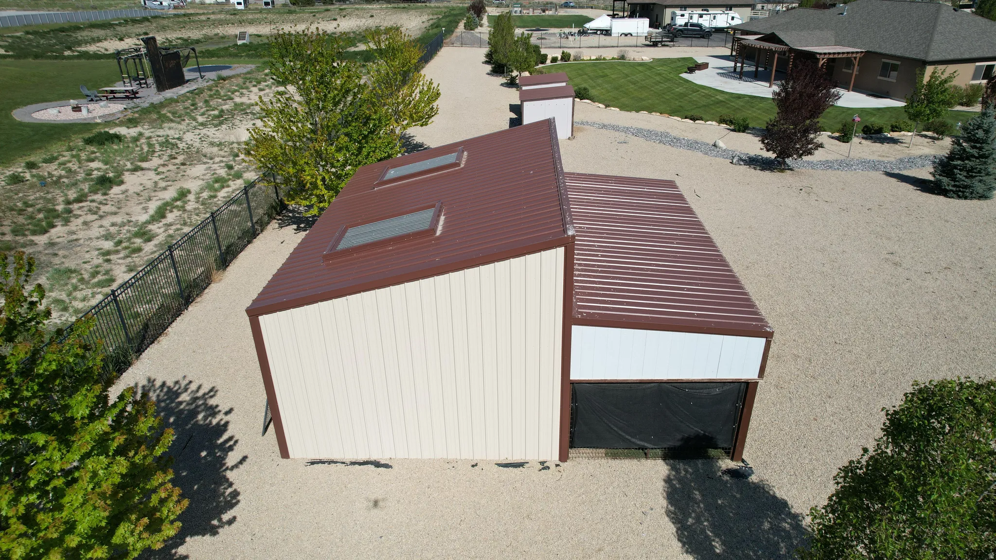 Metal-sided outbuilding featuring a brown corrugated roof with two skylights, a large roll-up door, and a gravel-covered surrounding area