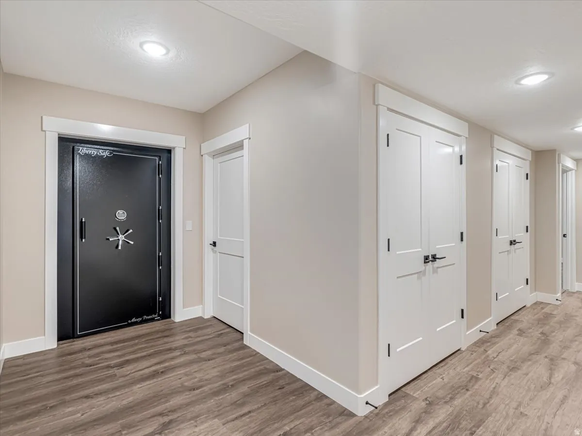 Hallway featuring wood-finish flooring, recessed lighting, and multiple white paneled doors with dark hardware