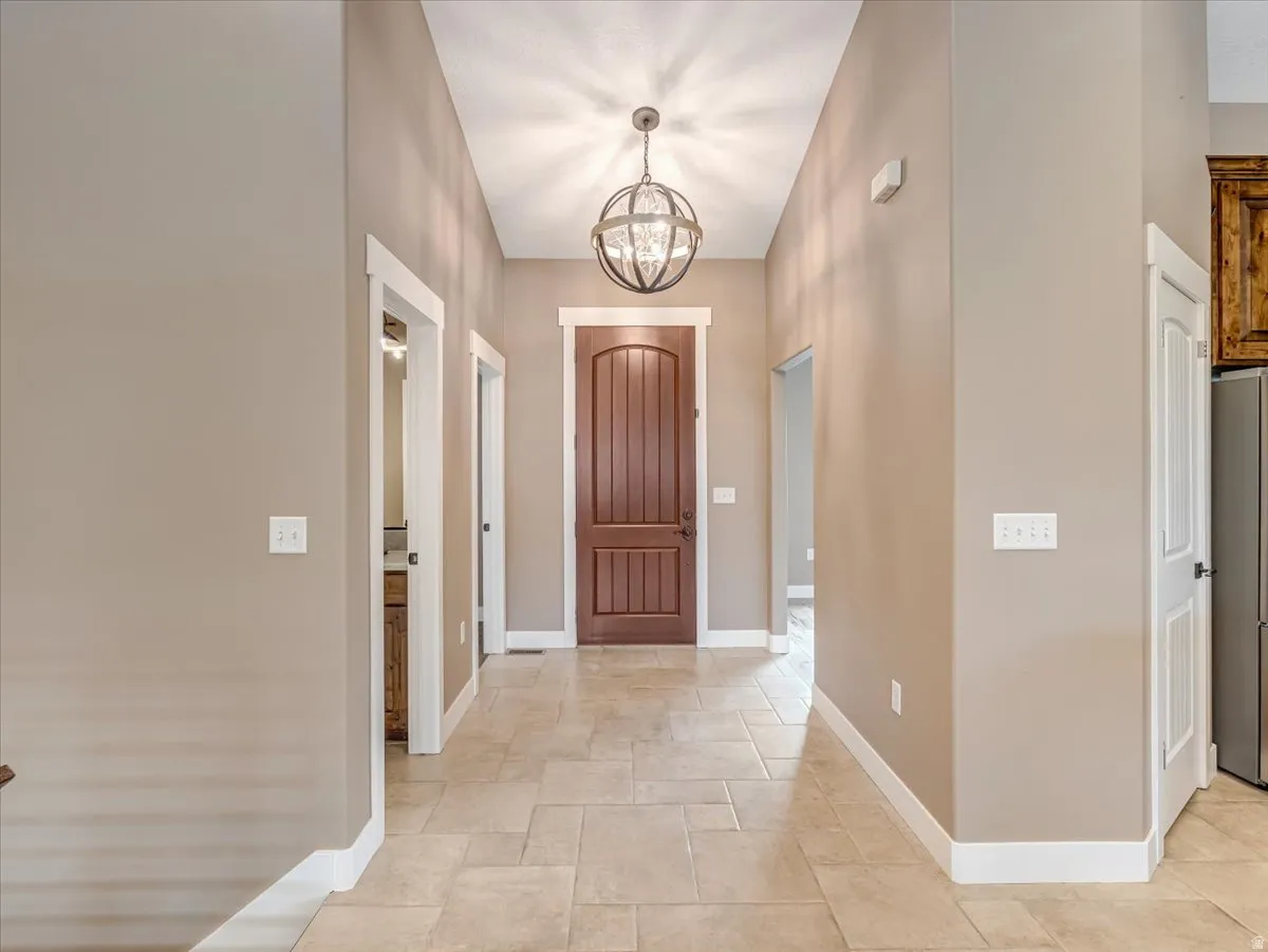 Gracious entry hall featuring an ornate spherical chandelier, a rich wood-paneled door with transom window, and expansive tile flooring