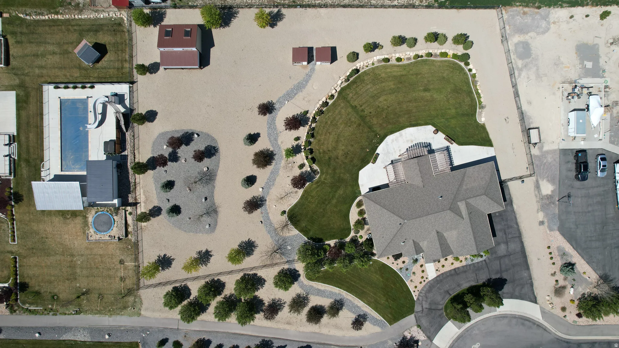 Expansive property featuring a large residence with a multi-gabled roof, an inground swimming pool, a separate outbuilding, an extensive gravel driveway, and distinct landscaped areas with mature trees and shrubs