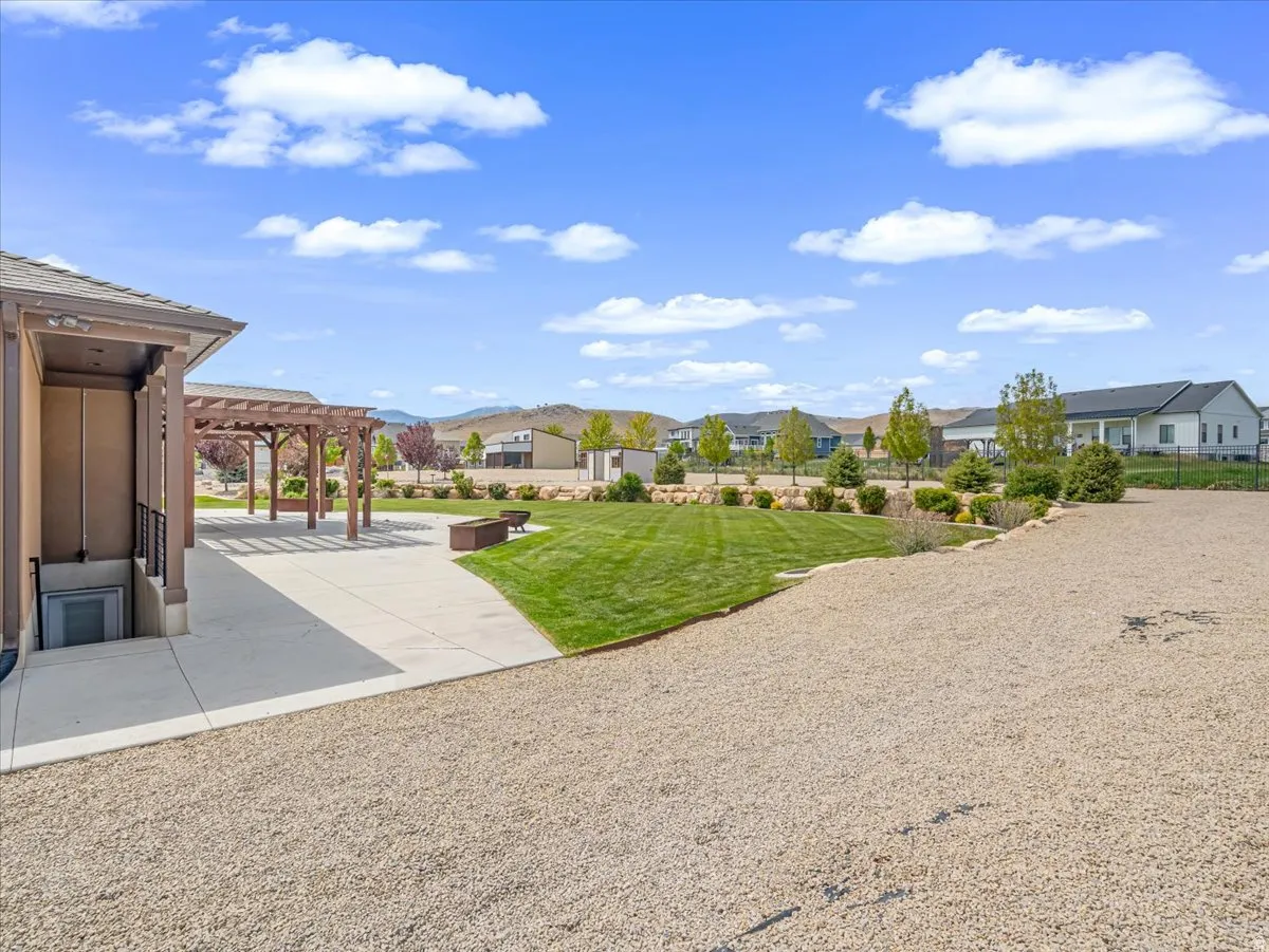 Expansive outdoor area featuring a pergola-covered patio, a manicured lawn, and a gravel surface