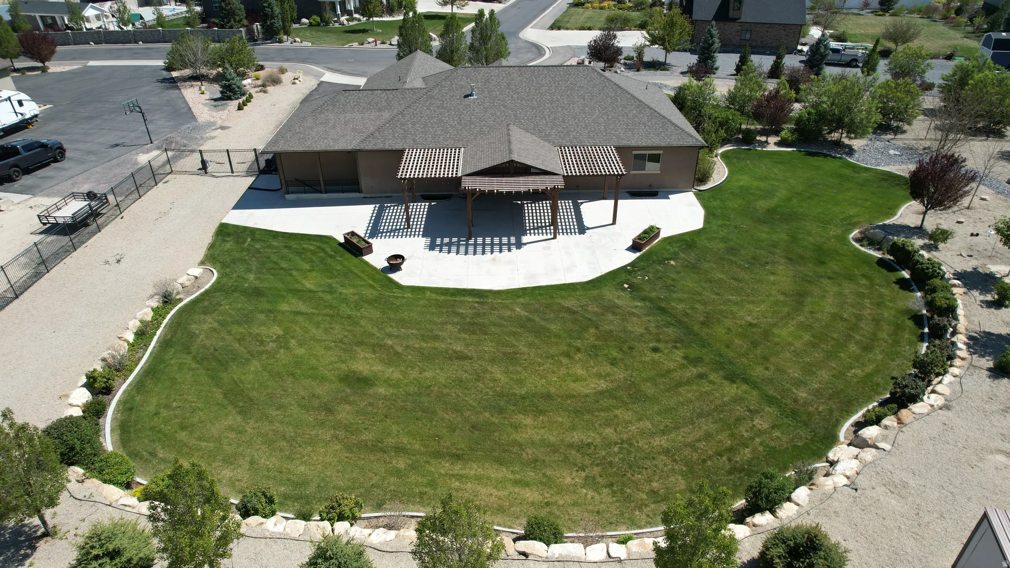Expansive lawn with manicured landscaping, featuring a paved patio, covered pergola, and a gravel perimeter